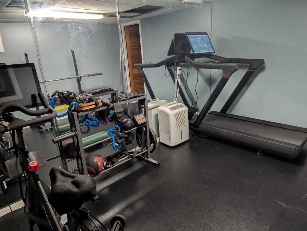 Picture of a hone gym with a treadmill, weights, and a Peloton.