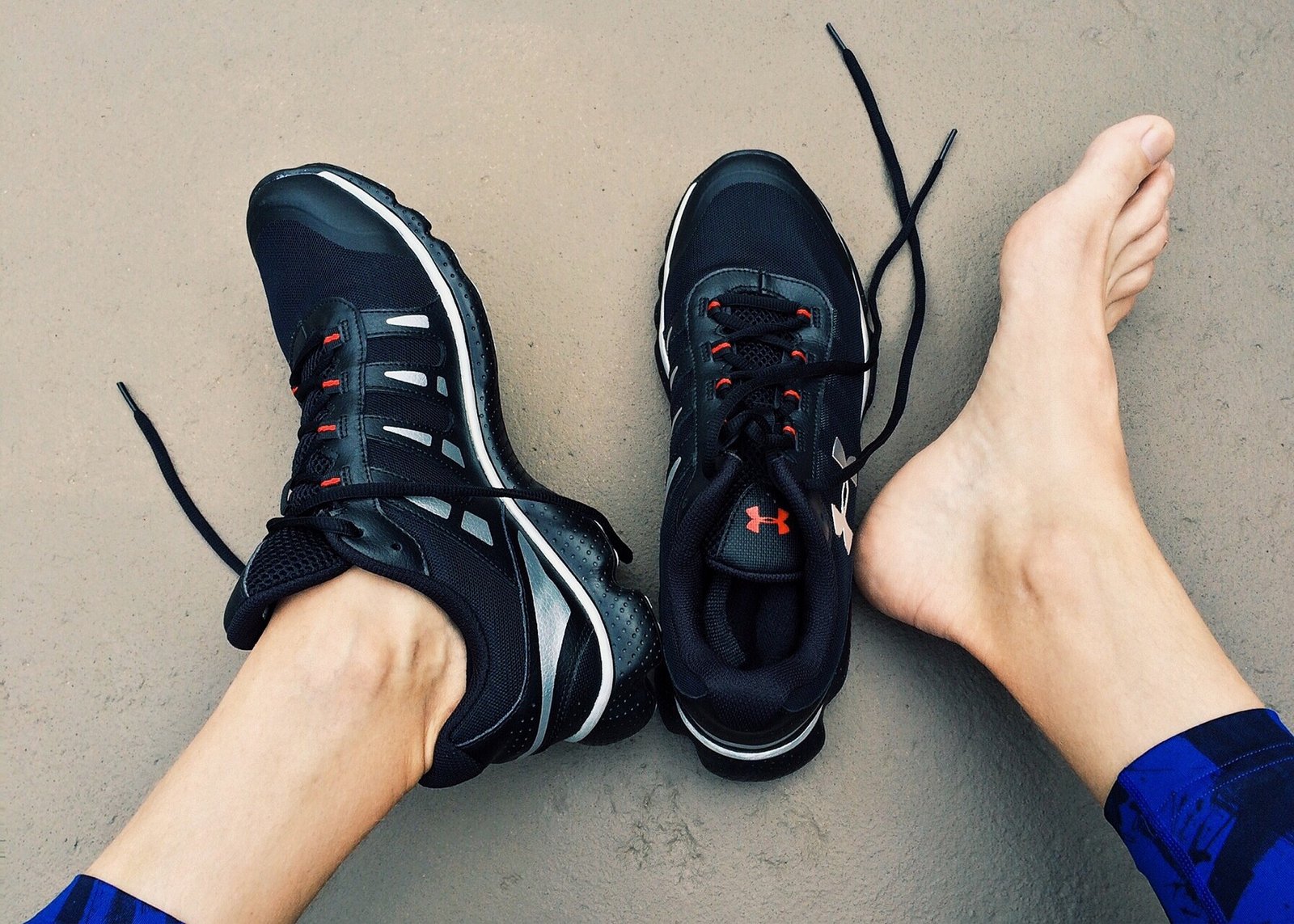 A runner looking at their feet, with one shoe on and one shoe off, wondering how many miles their running shoes last.