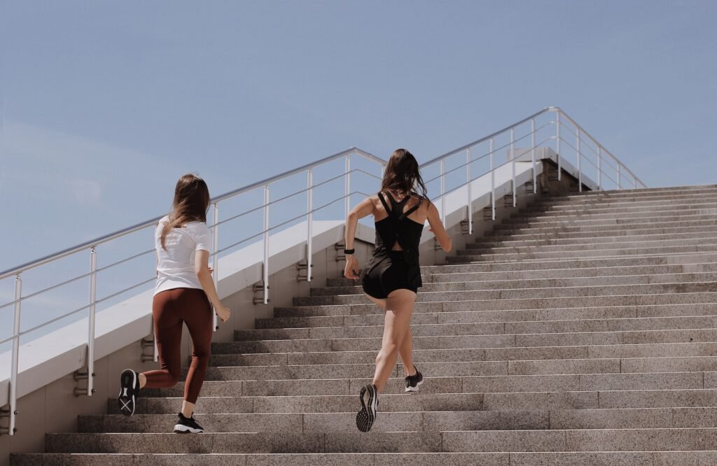 Two women, nearing the end of their recovery, running up steps after a marathon.