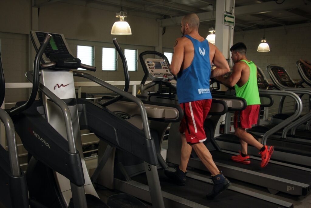 Two men running inside during the summer on a treadmill.