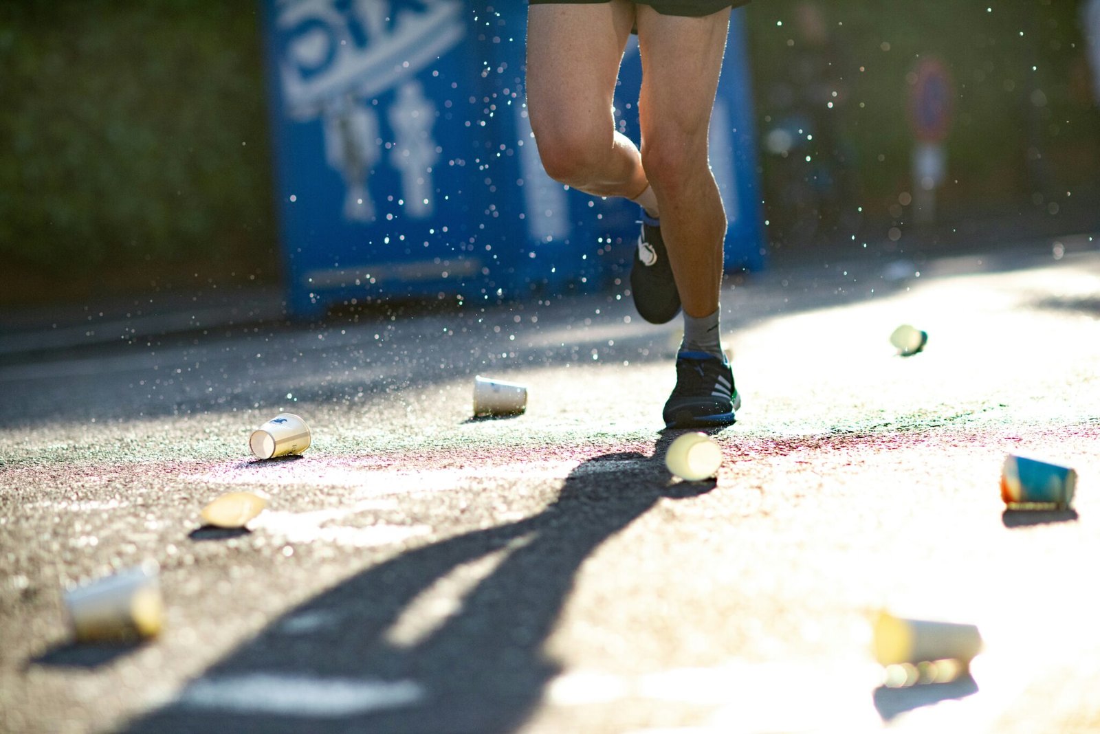 A photo of a person's legs, who is running a marathon, with cups of water on the ground around them.