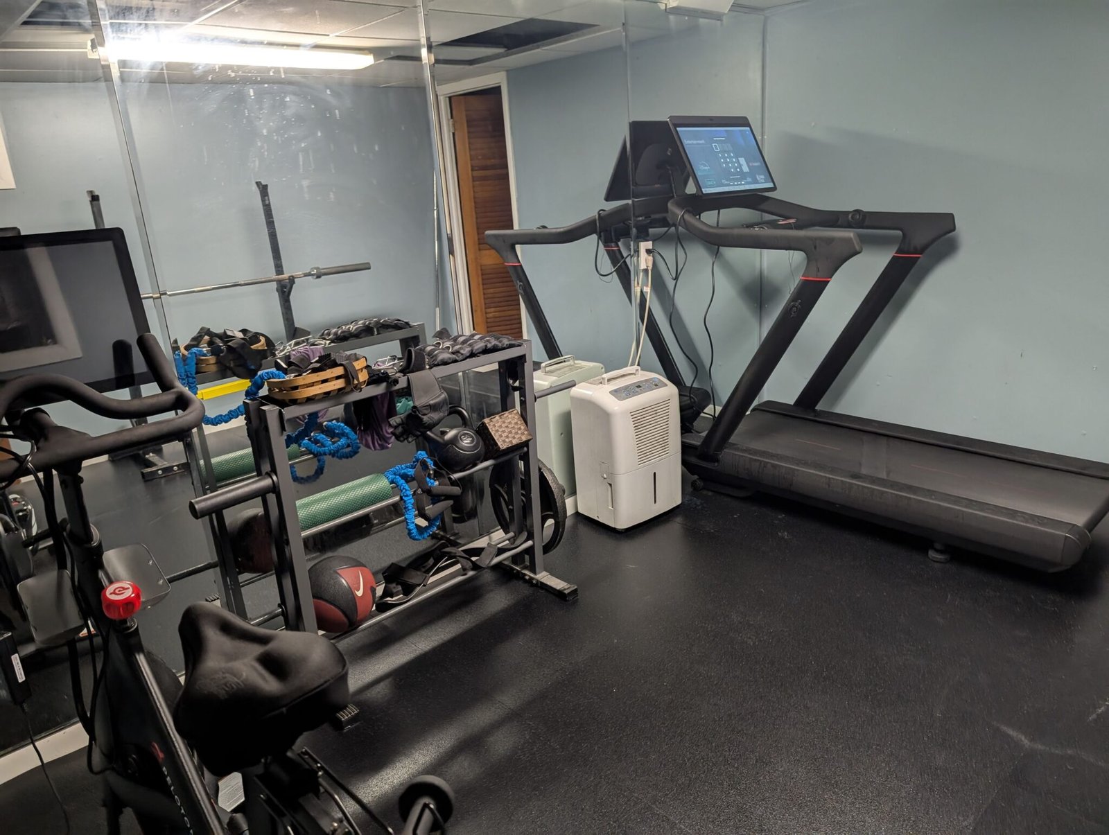 Picture of a hone gym with a treadmill, weights, and a Peloton.